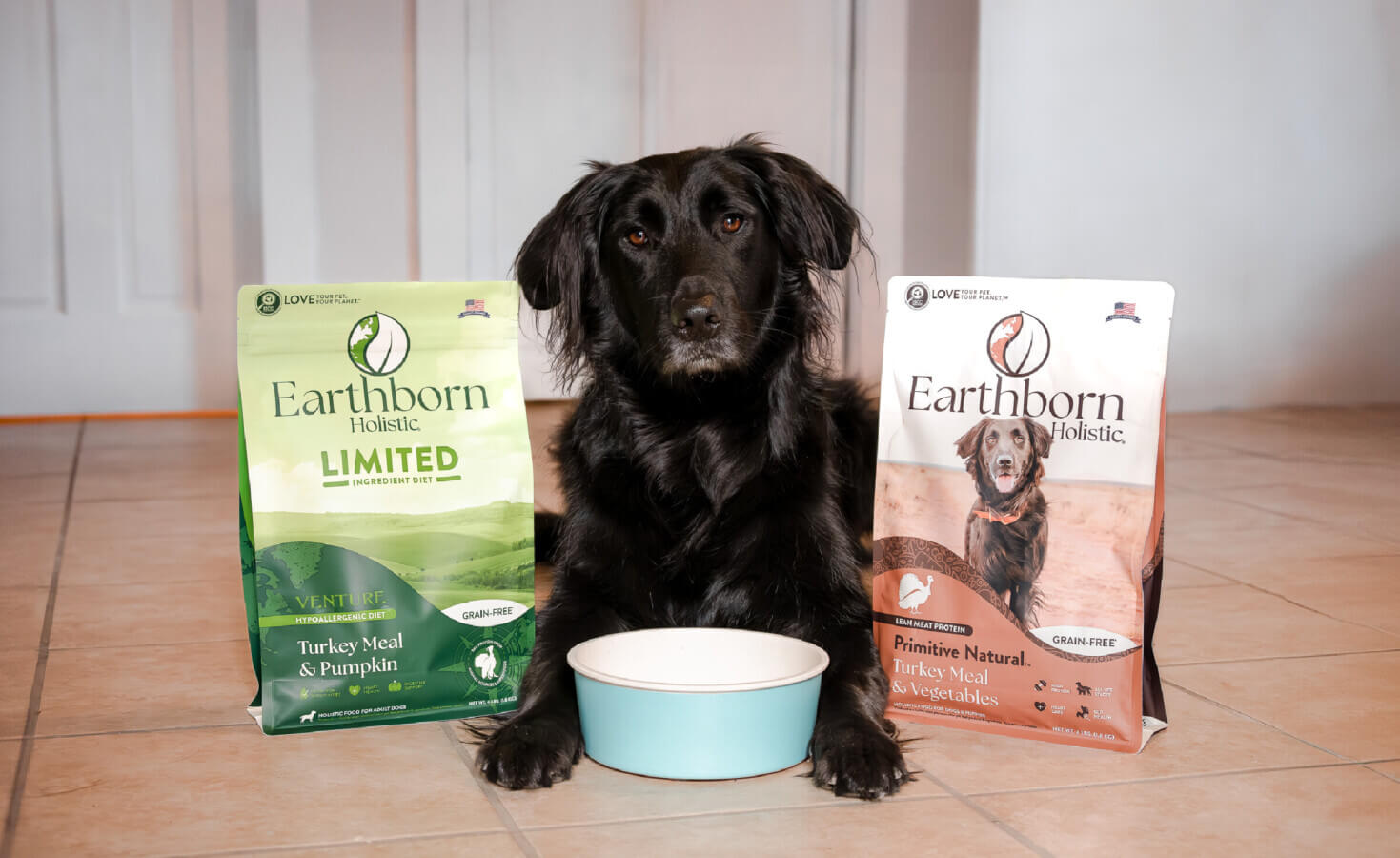 Dog lays with bowl between paws and bags of dog food on both sides of them