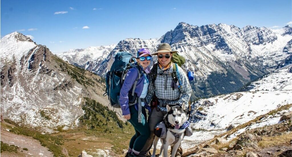 A couple and their husky stand at the top of Buckskin Pass in Colorado