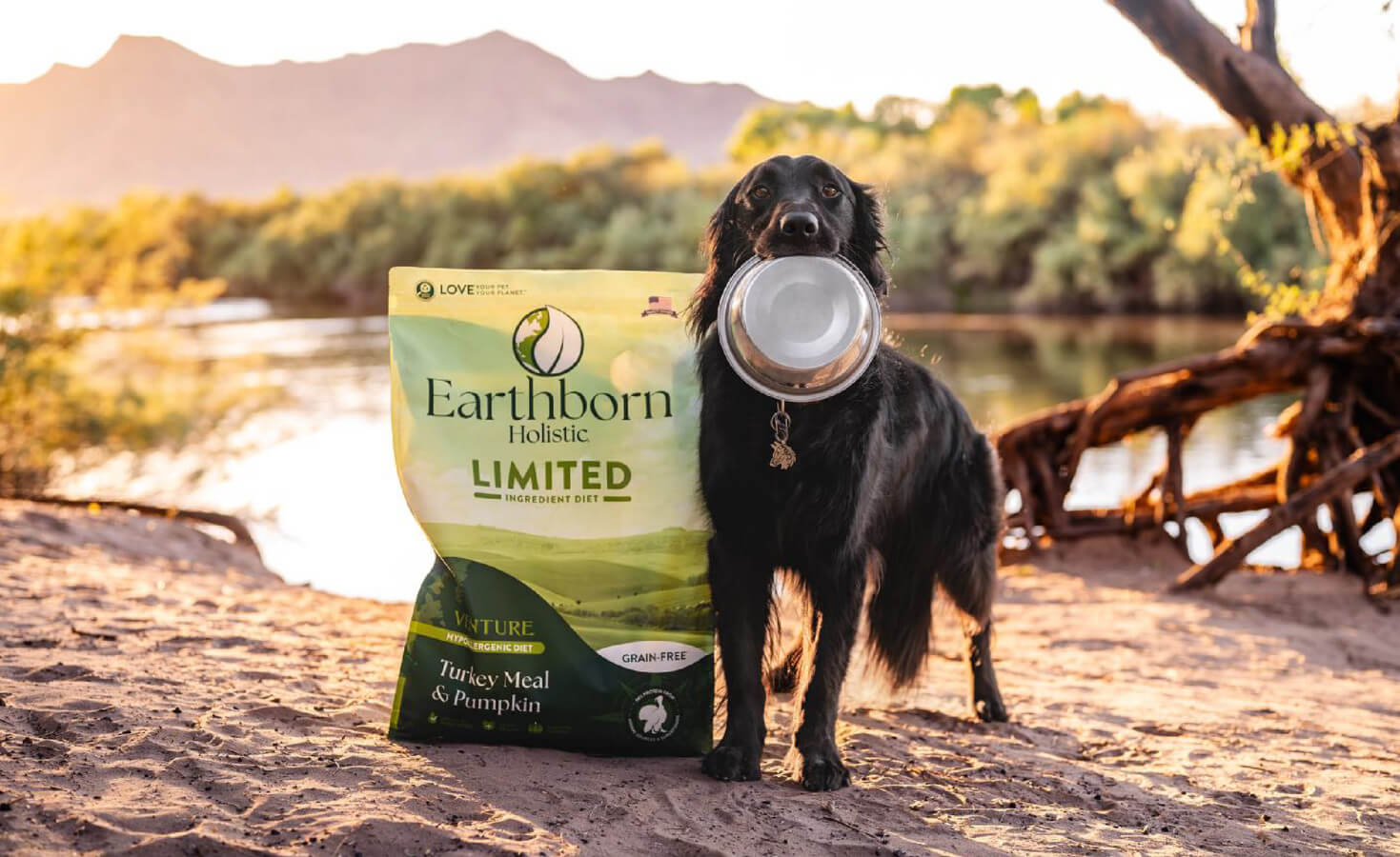 dog holds bowl in mouth next to bag of Earthborn dog food