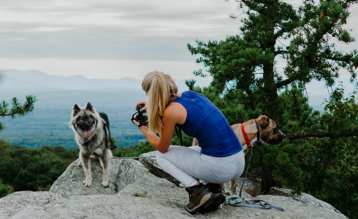 A female squats on a summit to get eye-level with her dog that she is taking a photo of