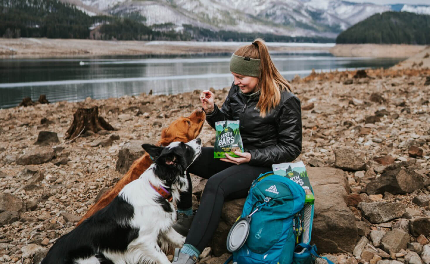 Person gives a dog an EarthBite next to a backpack