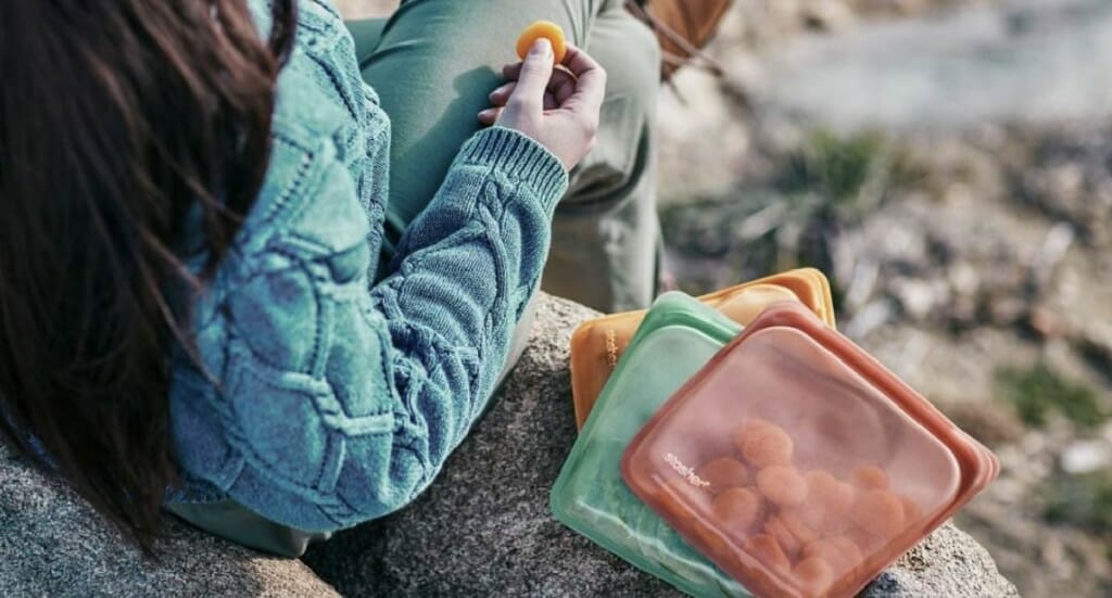A person sits outside eating a snack out of a Stasher bag