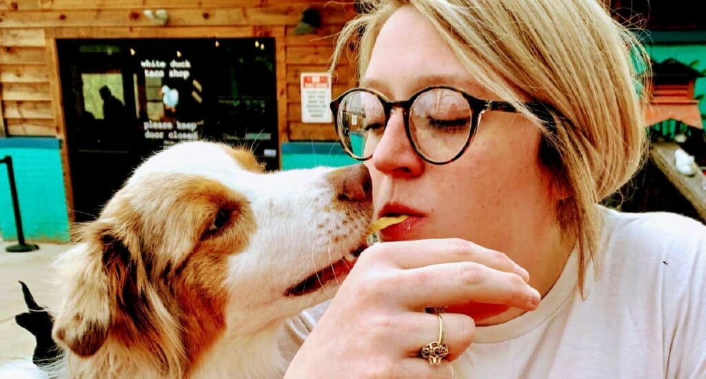 A woman eating a tortilla chip lets her dog take a bite