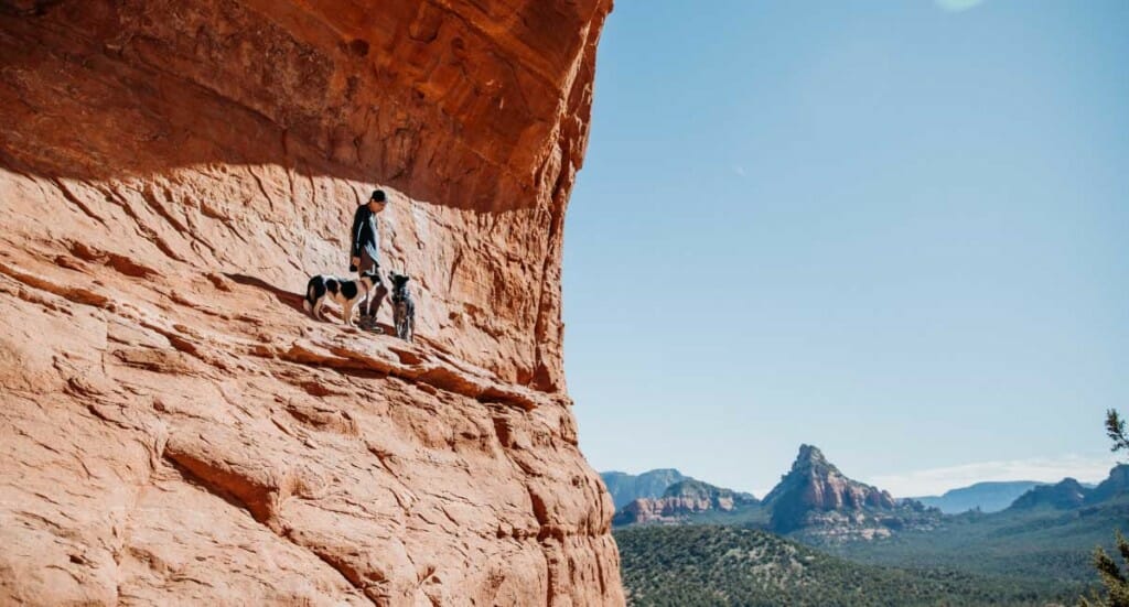 A woman and her two dogs walk alongside a cliff edge