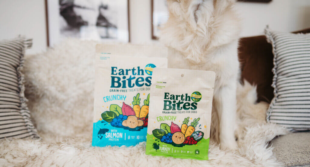 Dog sits on couch with two bags of EarthBites Crunchy