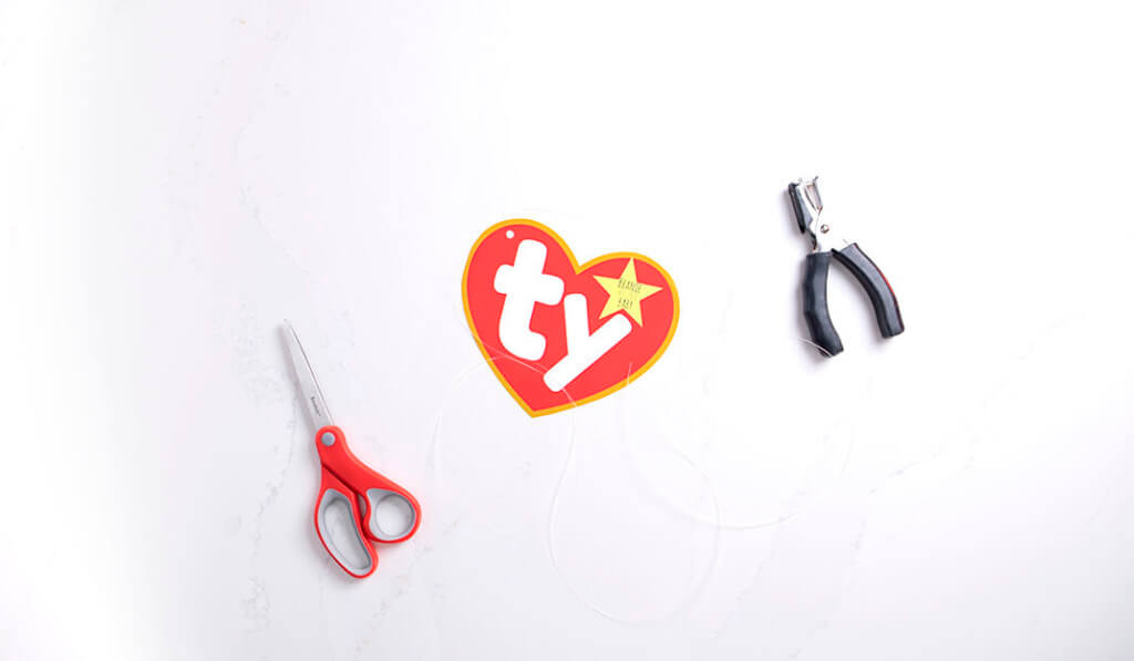 A flat lay of scissors, a hole punch, a Ty logo printout, and a piece of string