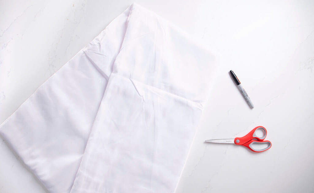 A flat lay of a white sheet, marker, and scissors to make a DIY dog ghost costume