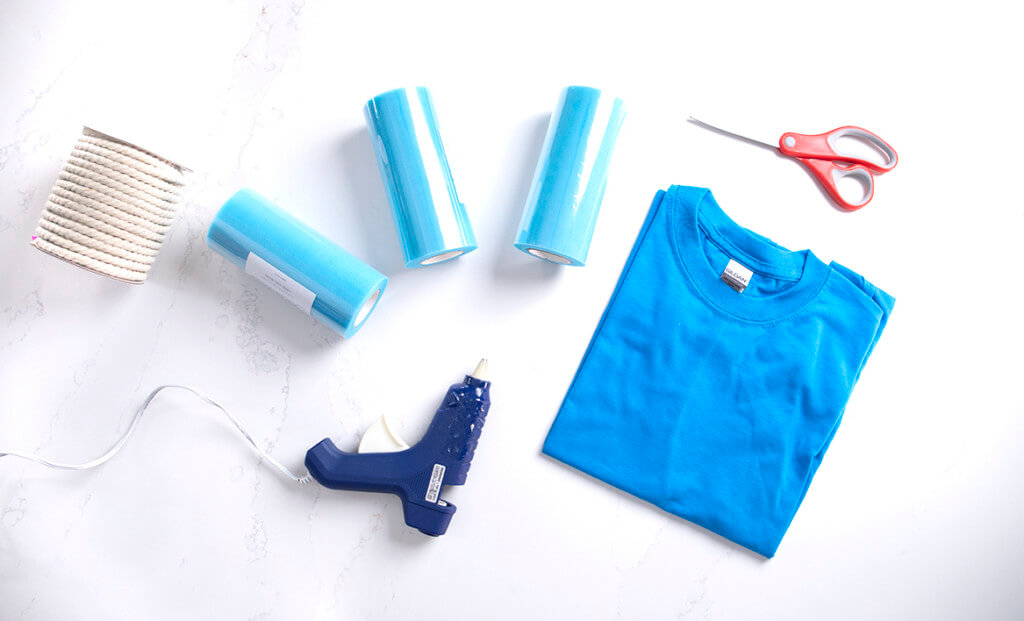 A flat lay of rope, blue tulle, a blue t-shirt, scissors, and a hot glue gun to make a DIY loofah Halloween costume