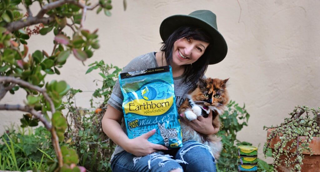 A woman holds her cat and a bag of Earthborn Holistic Wild Sea Catch cat food