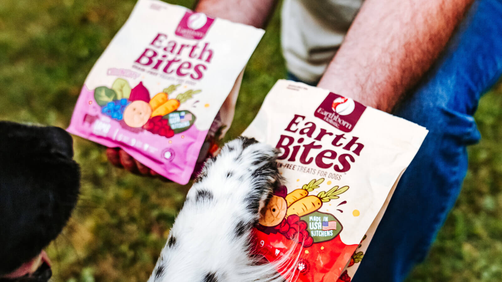 Person holds out two bags of EarthBites treats as dog puts paw on one bag