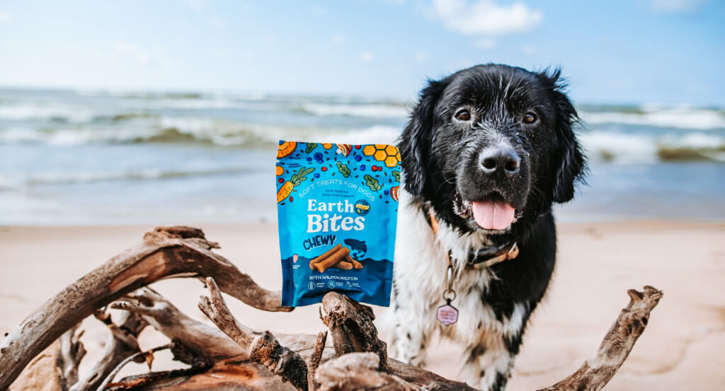 dog smiles next to a bag of EarthBites Chewy on a piece of wood