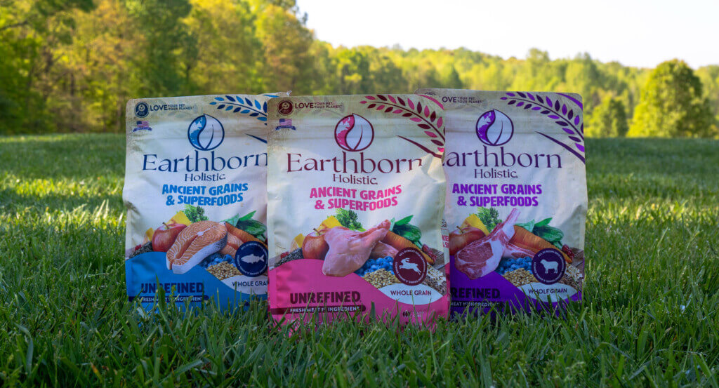 three bags of dog food sit in grass