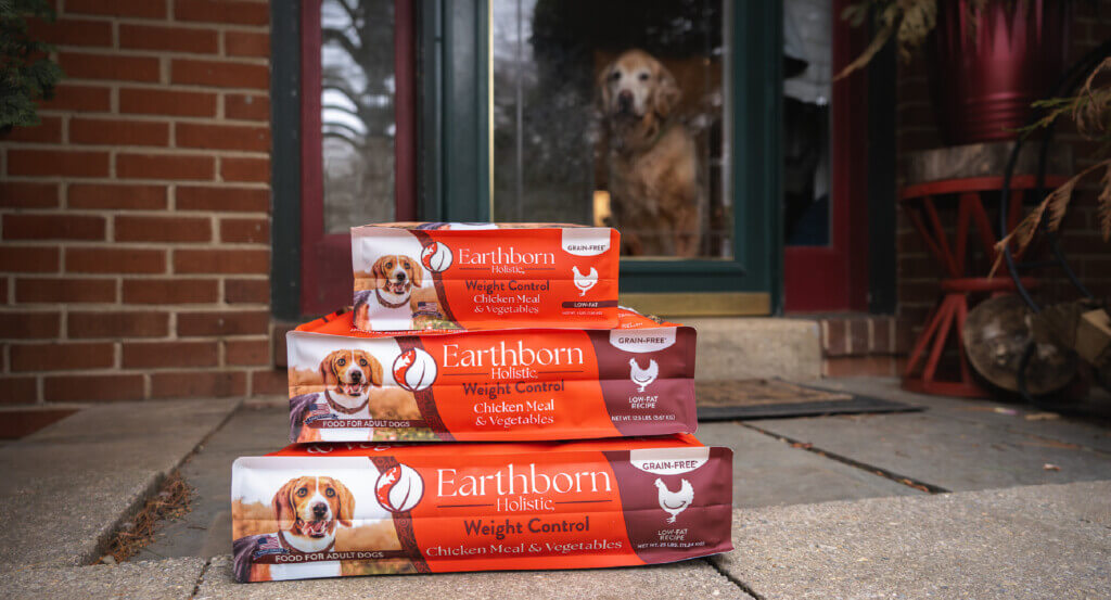 Three bags of Weight Control varying in size sit on top of each other as dog looks at them through door