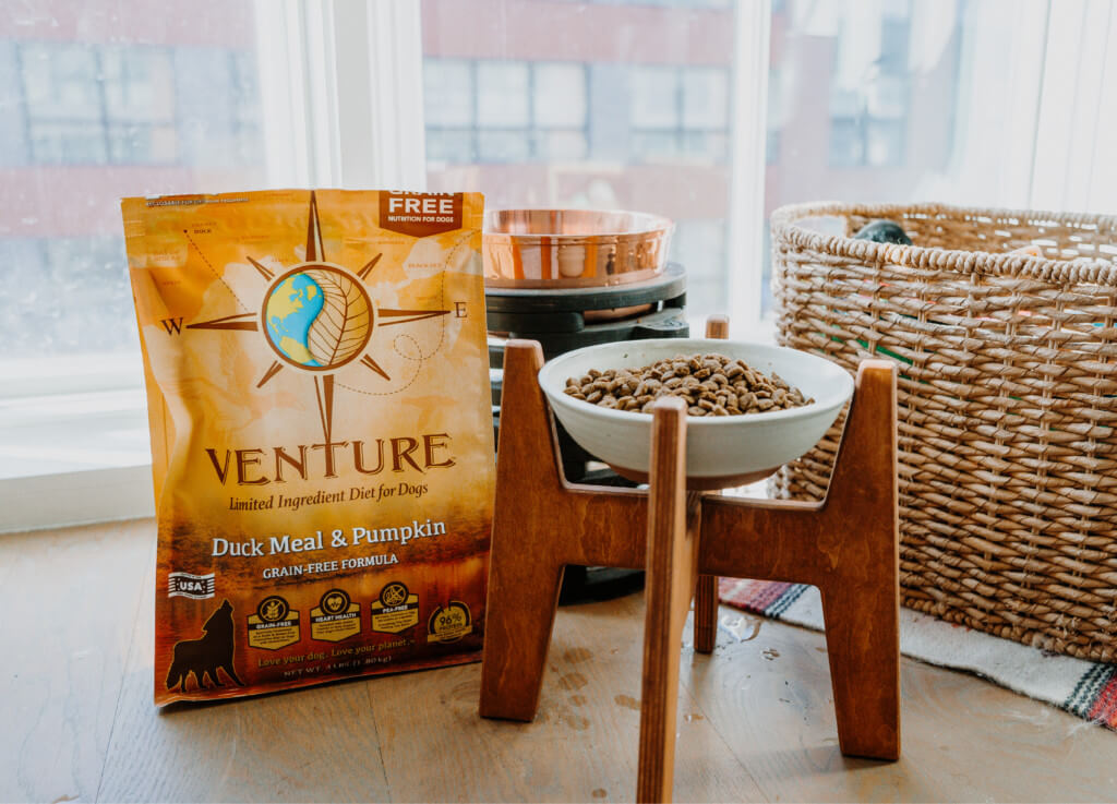 A bag of Venture Duck Meal & Pumpkin dog food sits next to a dog food bowl in an apartment