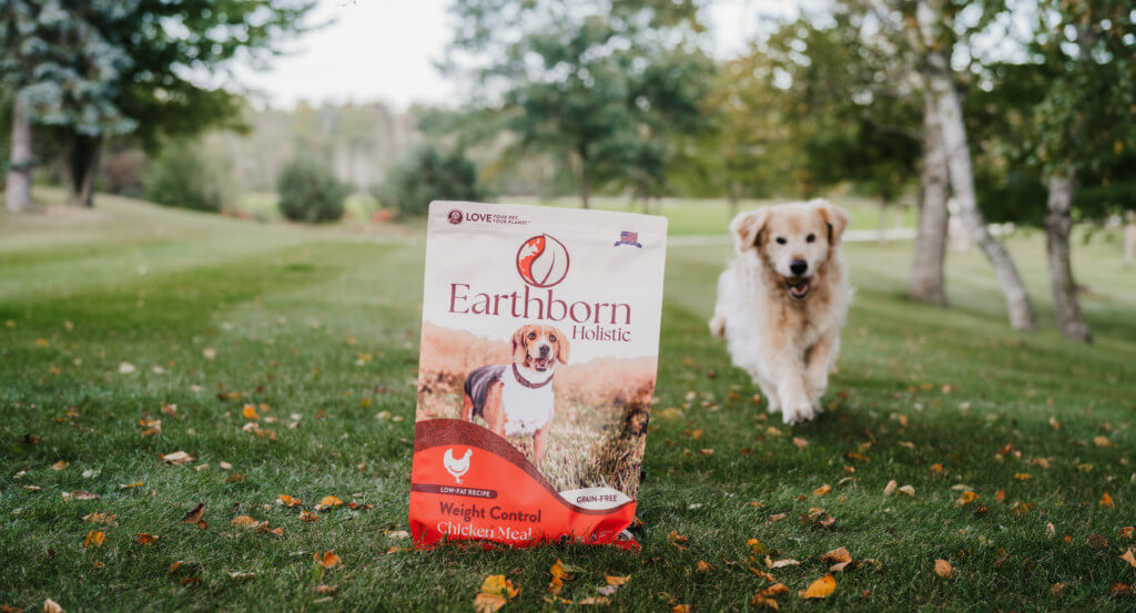 Dog runs towards a bag of Earthborn Holistic Weight Control dog food