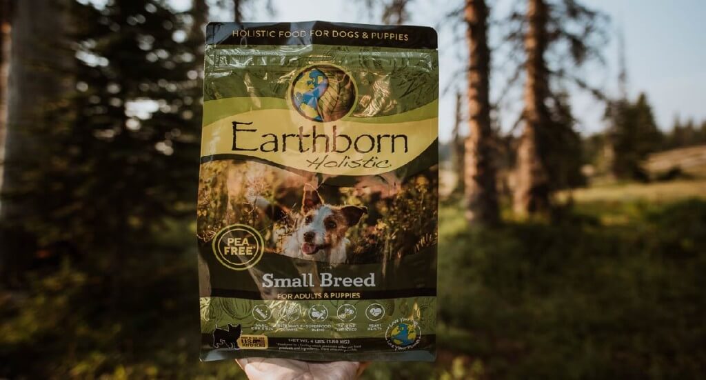 A hand holds a bag of Small Breed Earthborn Holistic in the woods