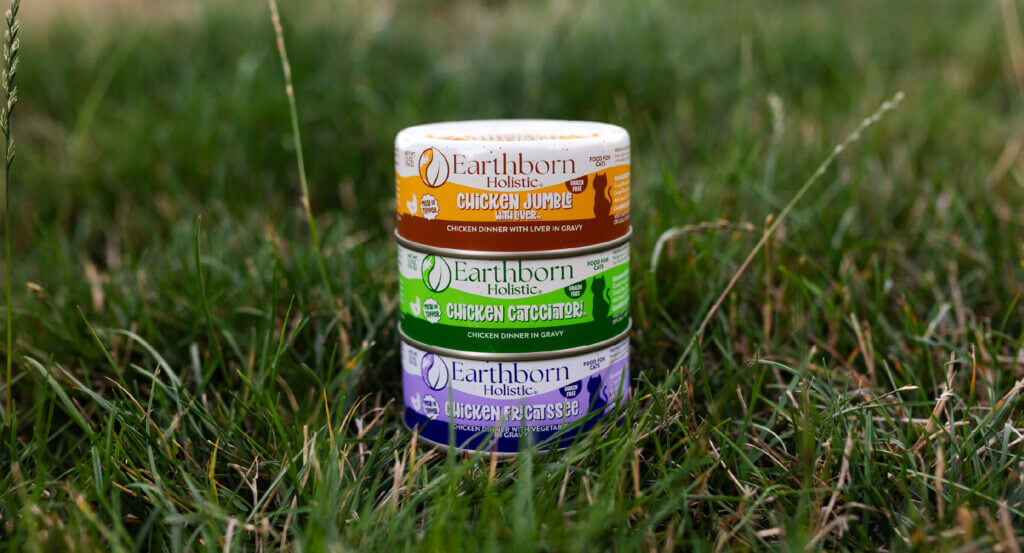 stack of 3 cat food cans sits in grass