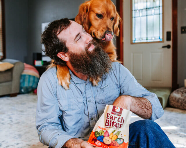 Person holds bag of treats as dog behind them licks lips
