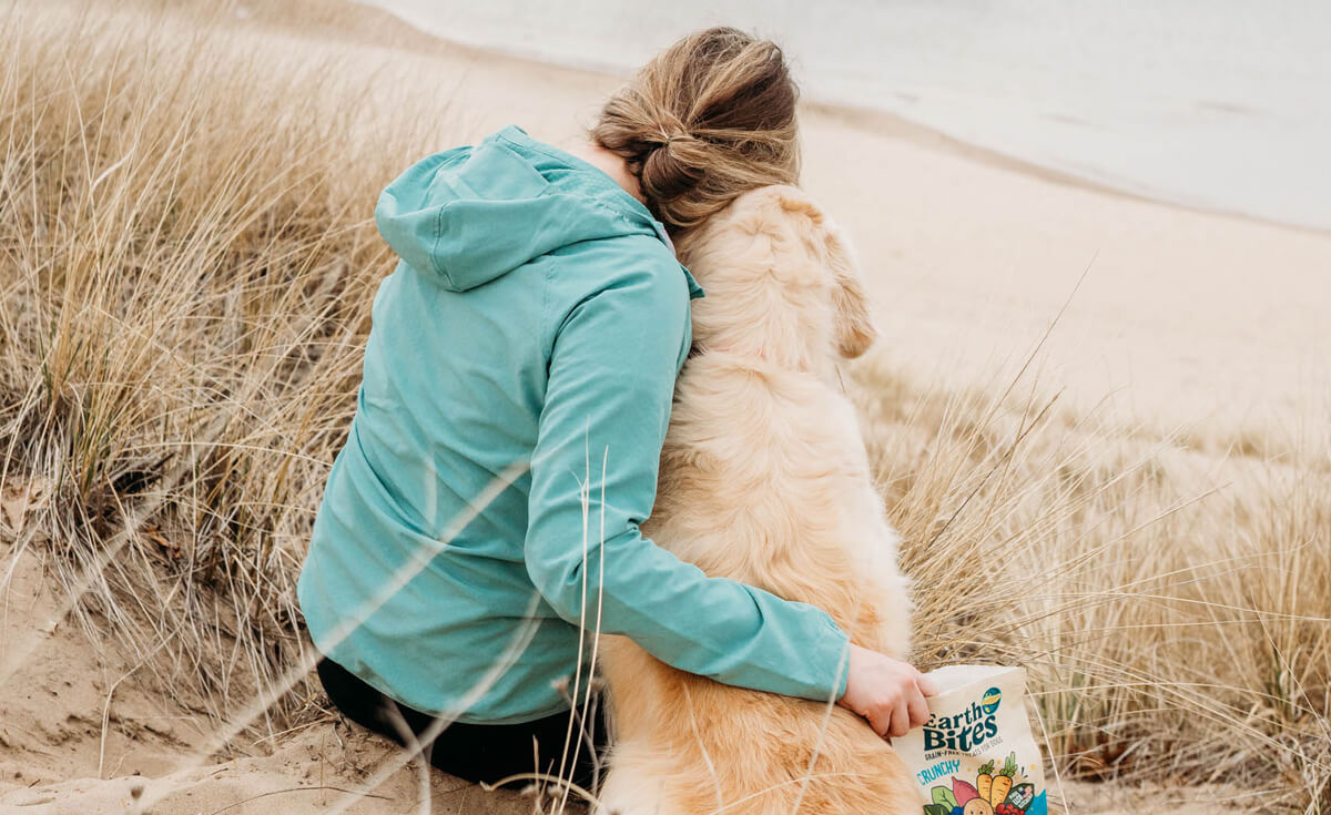 woman and dog snuggling with a bag of treats along the beach