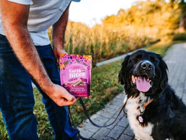 Dog smiles while person holds a bag of EarthBites Chewy