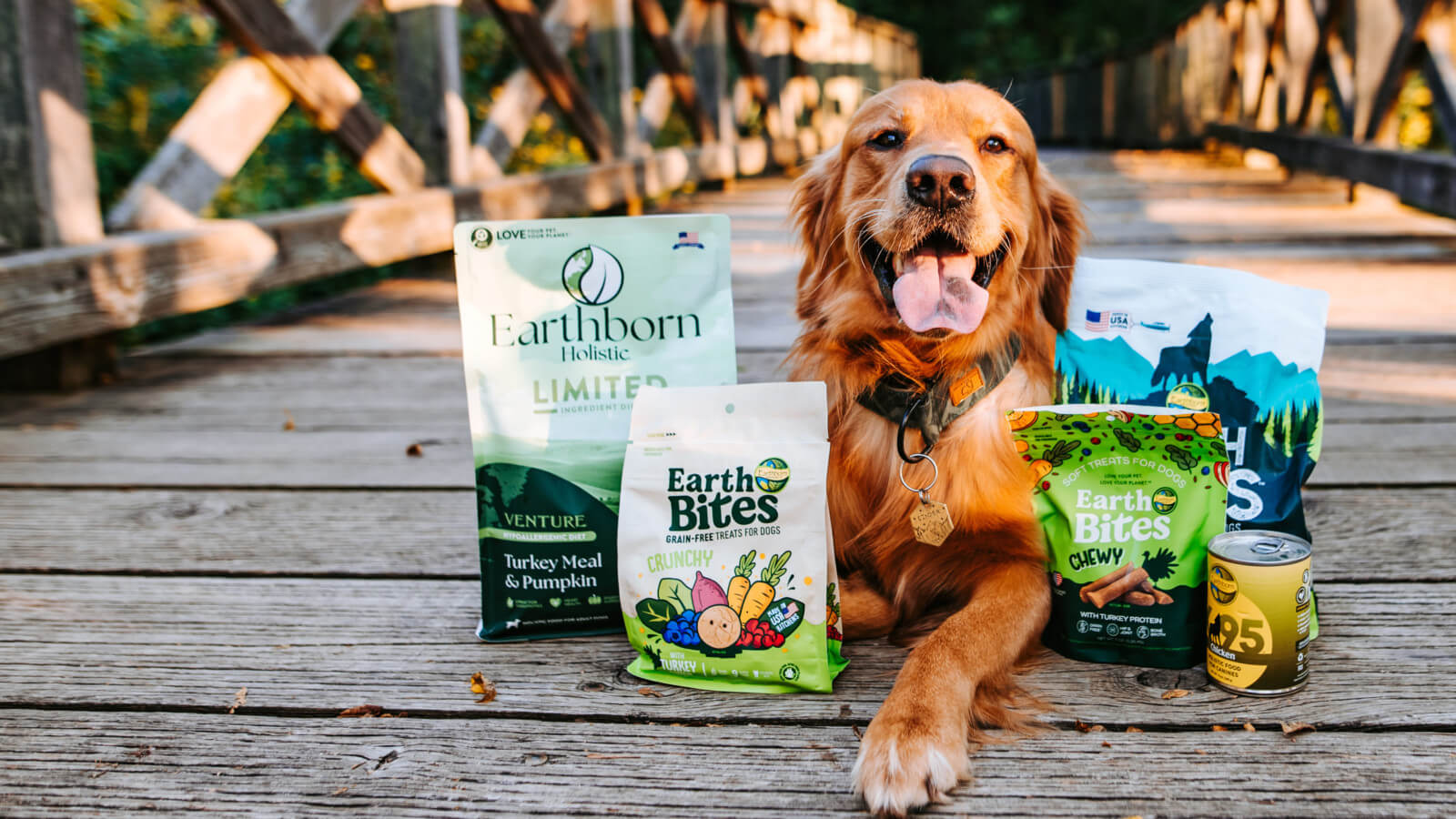 A golden retriever lays behind an assortment of Earthborn Holistic dog food and treats