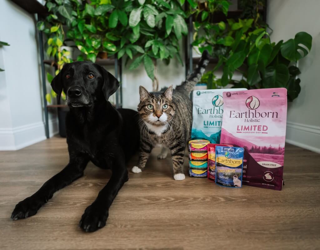 Dog and cat sit ext to a variety of Earthborn Holistic cat and dog food products