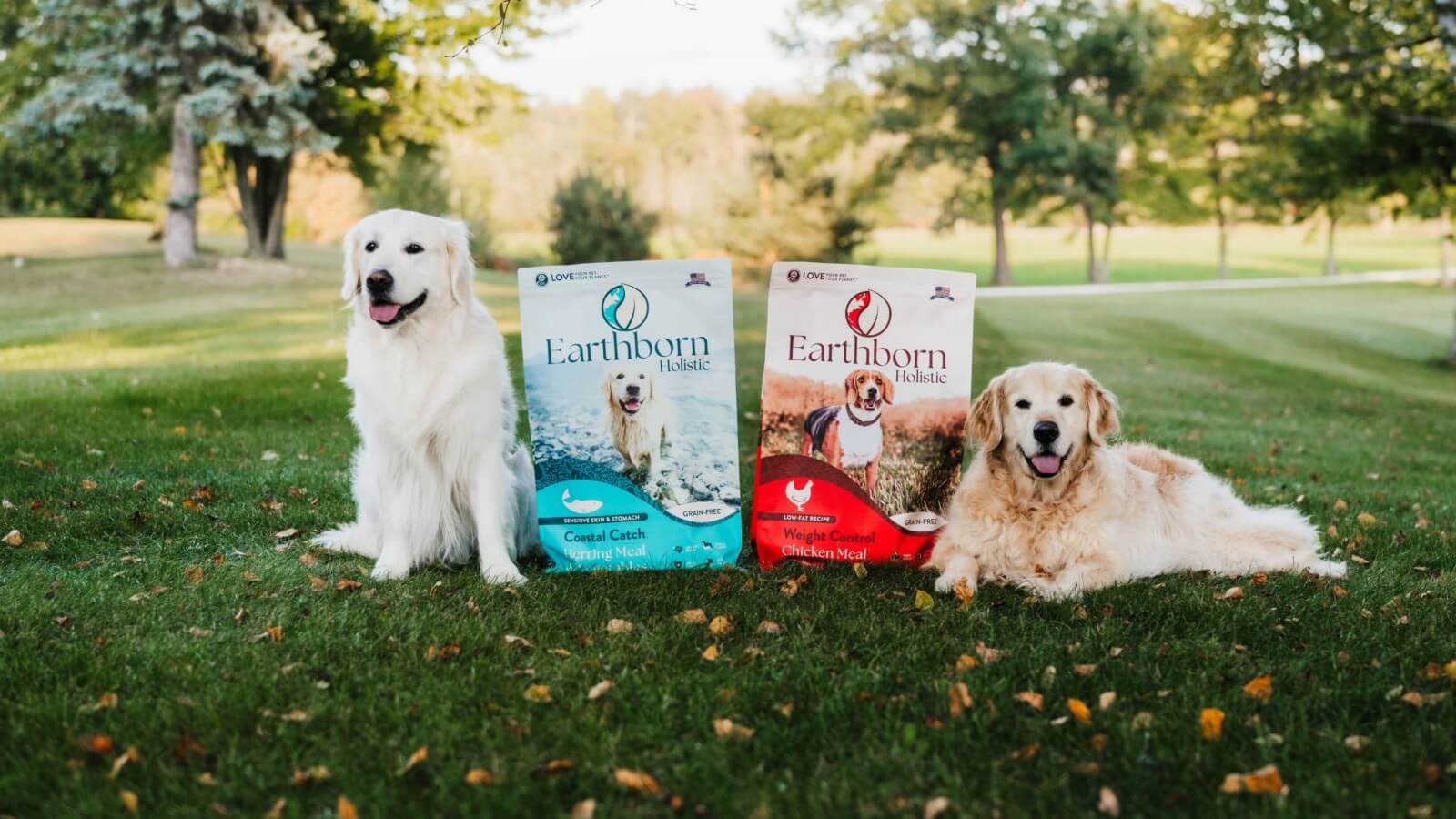 Dogs lay in grass with 2 bags of Earthborn Holistic between them