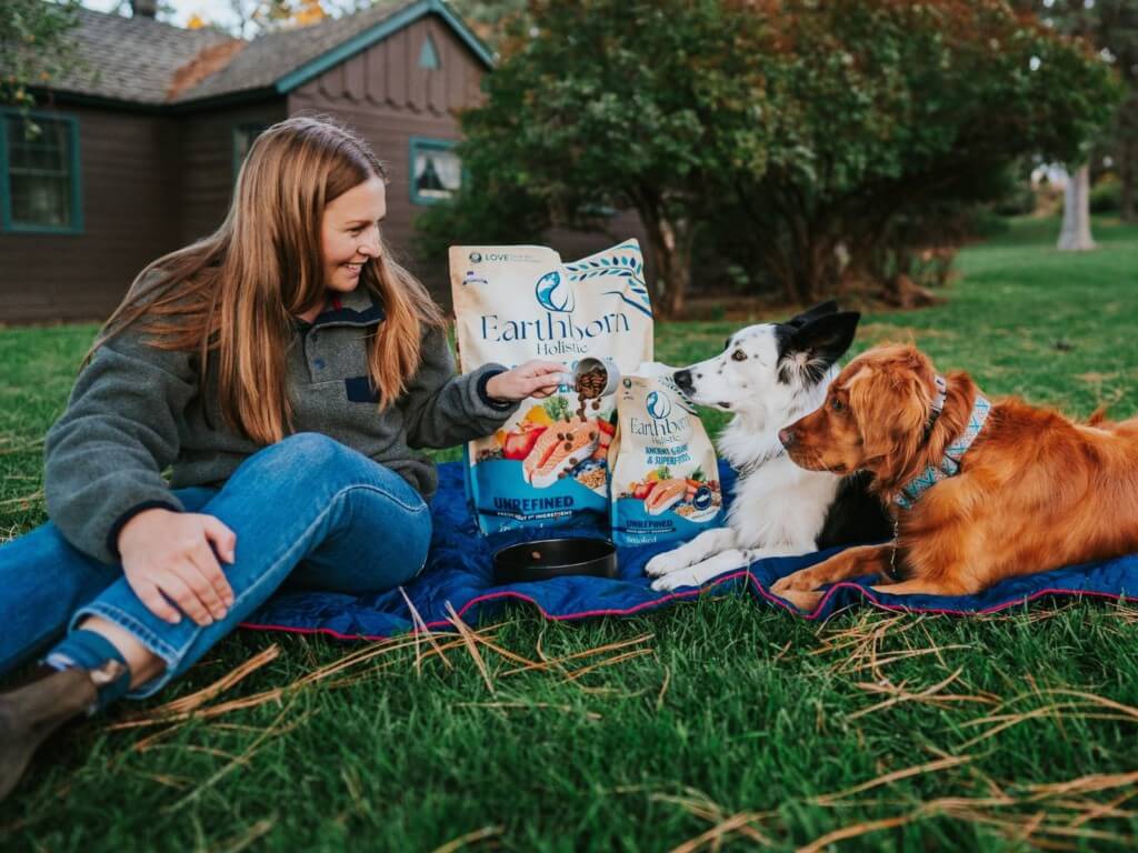 Woman pours a bowl of Earthborn Holistic Unrefined Smoked Salmon for her 2 dogs