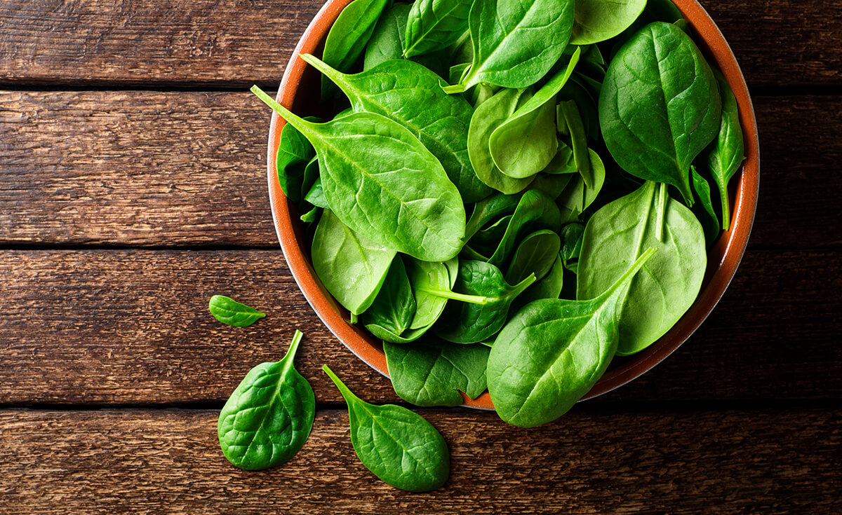 a bowl of spinach on a wooden table